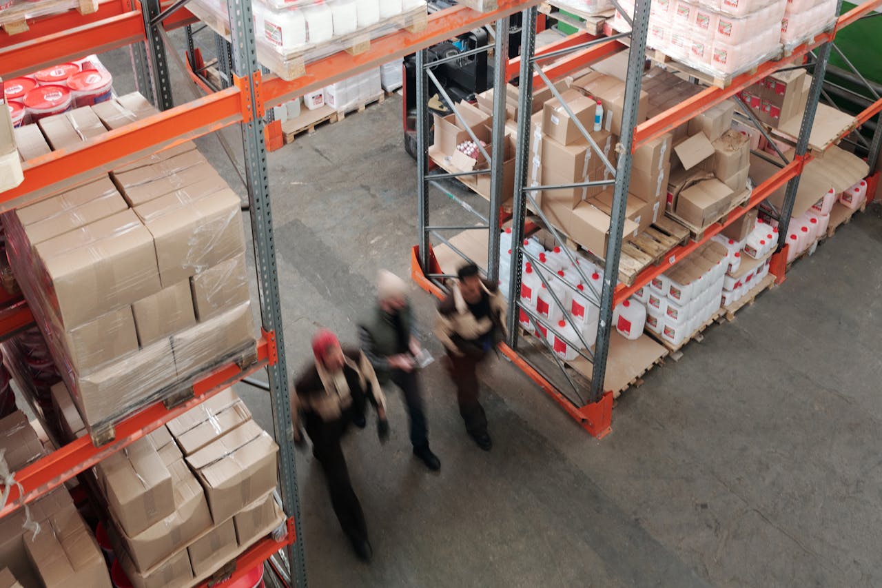 A high angle view of workers in motion in a busy warehouse with shelves full of boxes and packages.